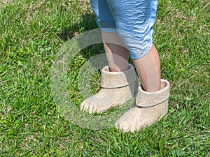 Cold summer. Women`s feet in felt boots on the green grass backg