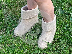 Cold summer. Women`s feet in felt boots on the green grass backg