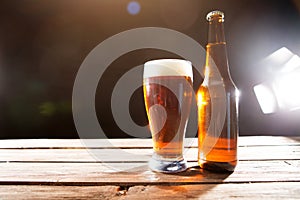 Cold tasty beer on hot summer day. Bottle and glass of beer on a wooden table against black background and copy space
