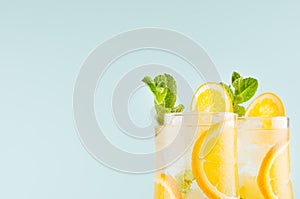 Cold tropical oranges juice in misted wineglass with sliced fruit, mint, ice cubes on blue background, closeup, top section, edge.