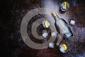 Cold vodka in shot glasses with lemon on stone background. Top view, copy space.