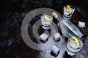 Cold vodka in shot glasses with lemon on stone background. Top view, copy space.