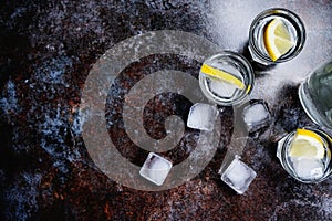 Cold vodka in shot glasses with lemon on stone background. Top view, copy space.