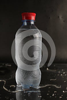 Cold water in a bottle on a black background. A bottle of water stands on a black background. Cool summer drinks