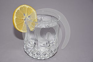 A cold water glass with lemon on white.