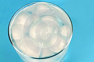 Cold water with ice cubes on blue background.