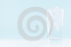 Cold water with ice in misted drinking glass on soft light blue background, white wood board.