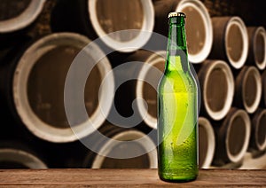 cold wet beer bottle in the cellar with vintage kegs