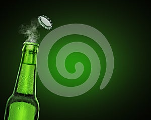 Cold wet open beer bottle with smoke on green background