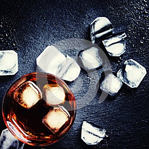 Cold whiskey with ice, black background, low key, top view