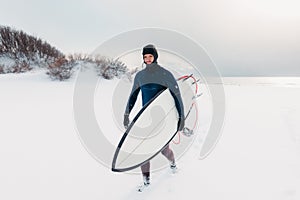 Cold winter and male surfer with surfboard. Snowy weather day with surfer in wetsuit