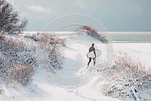 Cold winter and surfer with surfboard. Snowy day with surfer in wetsuit.