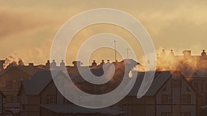 Cold winter in a village. Chimneys on roofs of snowy houses in the light of sunset