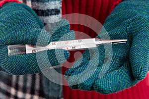 Cold woman hands with gloves holding thermometer