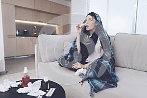 A cold woman sits on a light couch wrapped in a blue checkered whip. She sits plaid over her head