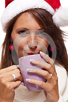 Cold young woman in a Santa hat sipping coffee tea