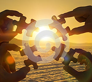 Collaborate four hands trying to connect a puzzle piece with a sunset background.