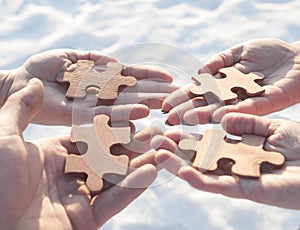 Collaborate four hands trying to connect a puzzle piece with a sunset background.