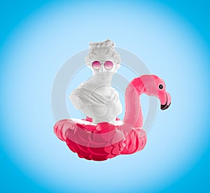 Collage of female head statuette with  inflatable flamingo and  pink glasses on  blue background. Summer travel poster concept