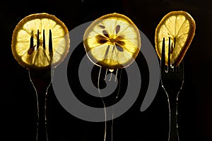 Collage of three slices of lemons on the fork on dark black background. silhouette of a fork in the back light. Drops of juice