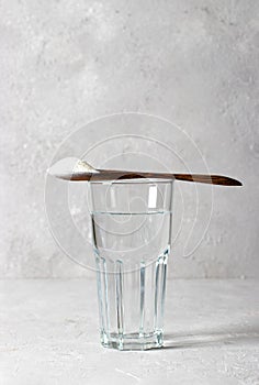 Collagen powder in spoon on glass of water on gray background. Healthy and antiage concept. Vertical format