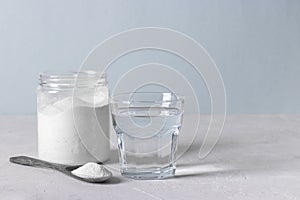 Collagen powder in spoon, glass of water and jar of powder on light blue background. Healthy and anti-aging concept