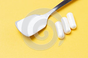 Collagen powder in a spoon and three white capsules on yellow background