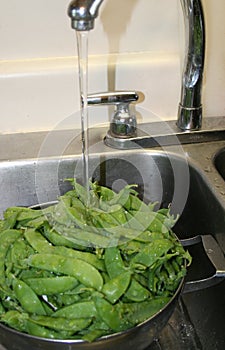 Collander of fresh snap peas in sink, rinsing under faucet