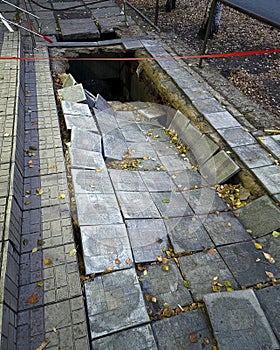 Collapse of the sidewalk from tiles into a deep pit. The concept of infrastructure destruction