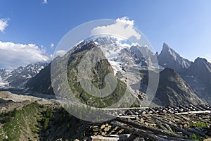 Collapsed roof of abandoned hut in the mountains. Beams of woods left on stones. European mountains with glacier and snow