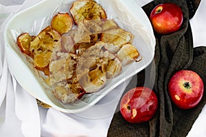 Collapsed soft baked apples in a white ceramic square shape on a special package. A white tablecloth is laid carelessly on the tab