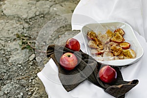Collapsed soft baked apples in a white ceramic square shape on a special package. A white tablecloth is laid carelessly on the tab