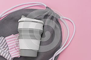 Collapsible silicone eco mug, folded reusable cloth menstrual pads and mesh bag on pink background