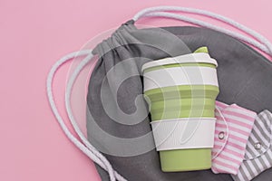 Collapsible silicone eco mug, folded reusable cloth menstrual pads and mesh bag on pink background