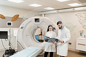 Colleague doctors discussing x-rays in the CT computed tomography scan room. Medical doctor intern girl is studying in