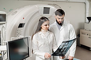 Colleague doctors discussing x-rays in the CT computed tomography scan room. Medical doctor intern girl is studying in