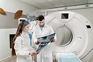 Colleague doctors discussing x-rays in the CT computed tomography scan room. Medical doctor intern girl is studying in