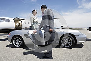 Colleague Holding Door Of Car For Colleague Near Private Aircraft