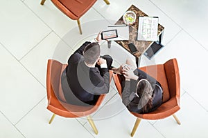 Businessman and businesswoman sitting in armchairs review the documentation, top view