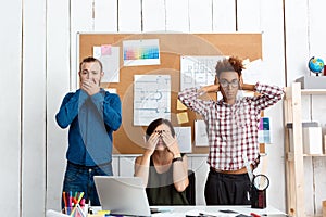 Colleagues closing mouth, eyes and ears with hands in office. See-hear-speak no evil variation.