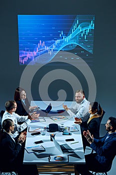 Colleagues in corporate setting analyze market data while examining a digital stock chart displayed on a monitor.