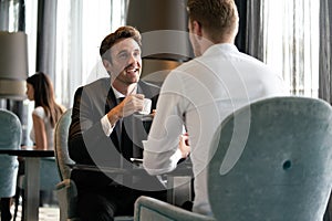 Colleagues and friends. Two cheerful businessmen drinking coffee and talking to each other