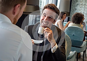 Colleagues and friends. Two cheerful businessmen drinking coffee and talking to each other