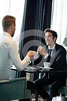Colleagues and friends. Two cheerful businessmen drinking coffee and talking to each other