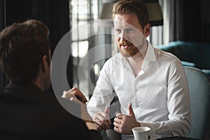 Colleagues and friends. Two cheerful businessmen drinking coffee and talking to each other