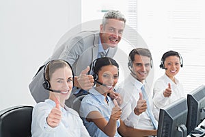 Colleagues with headsets using computers while gesturing thumbs up