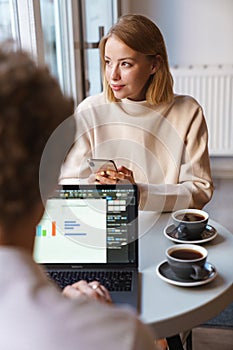 Colleagues sit in cafe using laptop computer