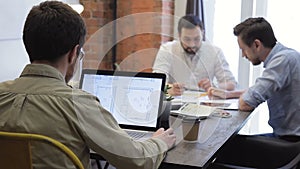 Colleagues sit at the table and work every with their information in office.