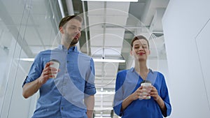 Colleagues walking with paper cups in office. Business woman and man talking