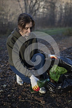 Collect garbage in the fall in a trash bag. A woman in the forest saves nature from destruction. The world`s